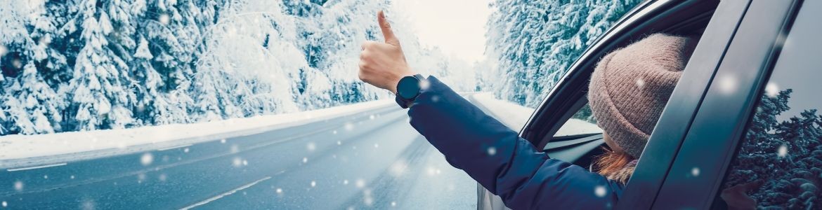 mujer haciendo gesto feliz en coche con carretera nevada